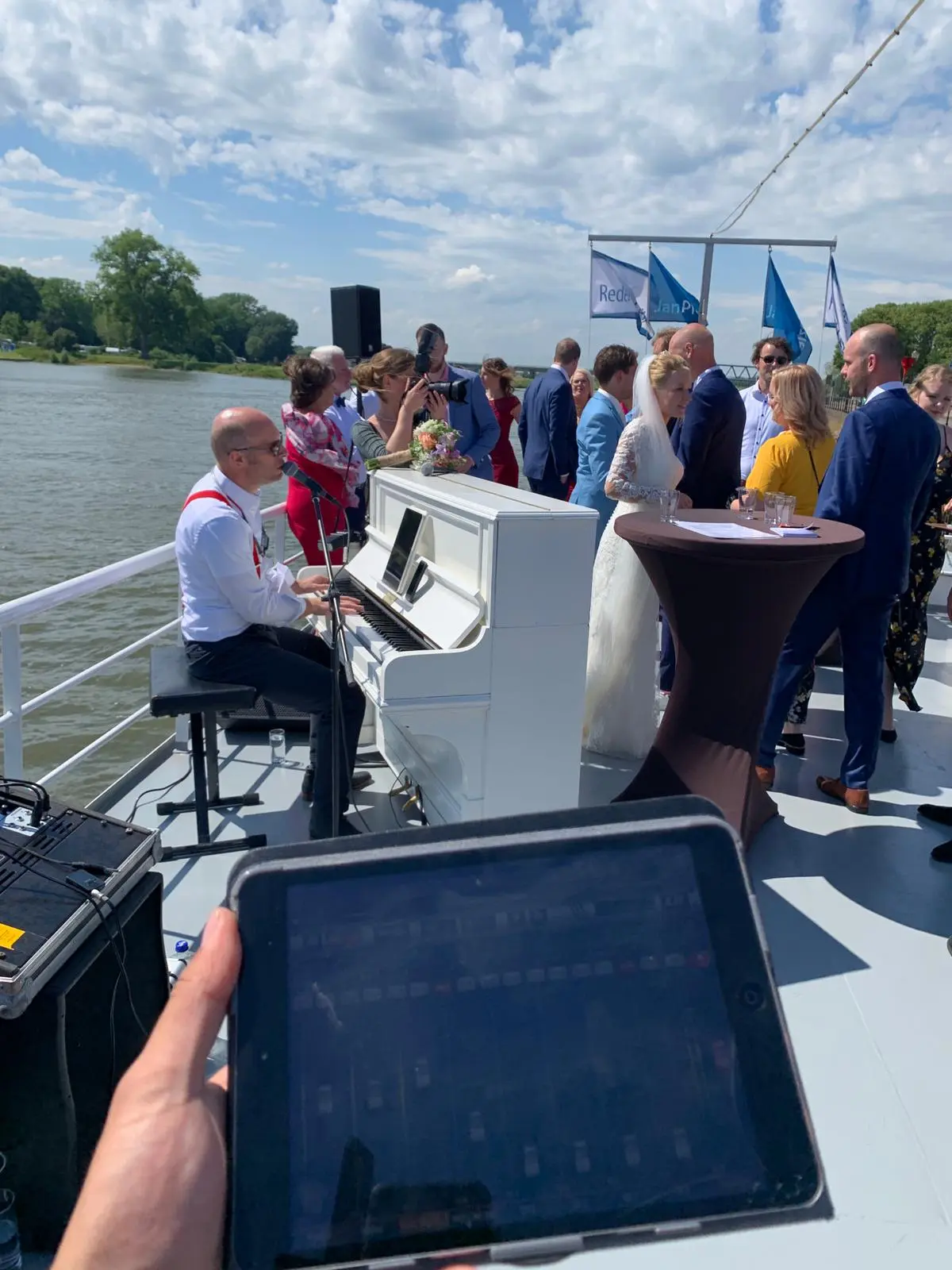 Live pianomuziek tijdens een bruiloft op het water, met gasten die samenkomen rond de piano